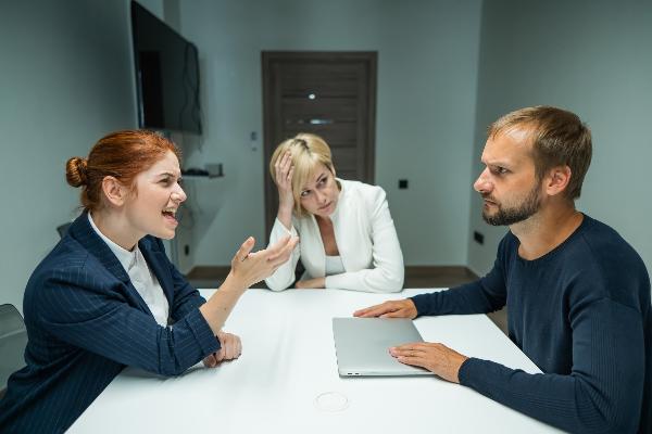 Business meeting conflict with arguing colleagues and mediator, tense discussion at office table with laptop