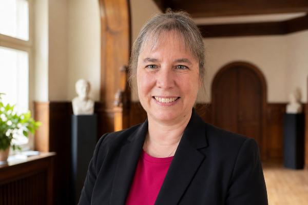 Professor Gitta Kutyniok steht in einem Gang. Hinter hier sind Holzinterieur und Büsten zu sehen. Sie blickt freundlich in die Kamera und trägt eine dunklen Blazer und einen pinken Pullover.