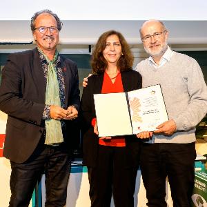 Cecilia Scorza und Harald Lesch mit Professor Stephan Jolie, Vizepräsident der Johannes-Gutenberg-Universität Mainz. Cecilia Scorza steht in der Mitte und hält die Urkunde zum Preis.