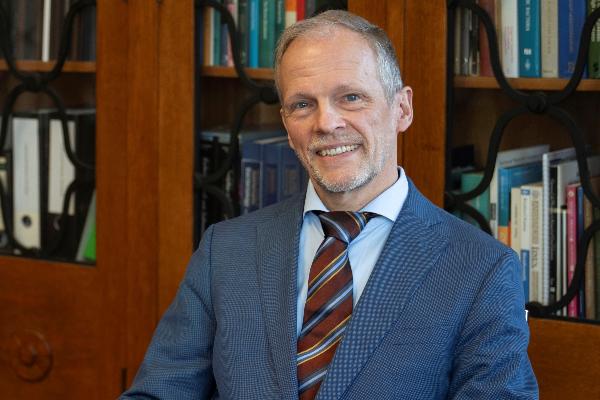 Professor Overmann in a business suit standing in front of bookshelves in an office
