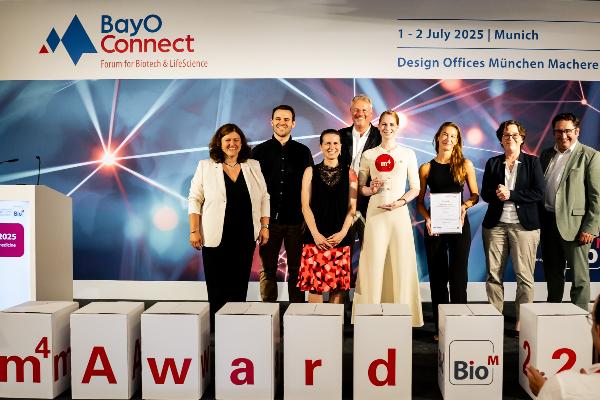 Gruppe von Preisträgern beim m⁴ Award 2025 in München auf der Bühne mit Urkunde und Trophäe, vor BayO Connect Banner.