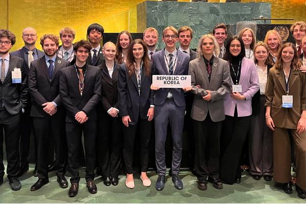 Gruppe junger Delegierter in formeller Kleidung posiert mit einem Schild „Republic of Korea“ im Plenarsaal der UNO.