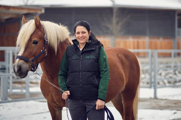 The new head of the Horse Clinic at LMU, Professor Angelika Schoster, in the clinic´s wintry outdoor area. Next to her is a horse with a blonde mane.