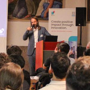 Dr. Philipp Baaske spricht vor Publikum in der Fresco-Halle der wirtschaftswissenschaftlichen Fakultäten der LMU über „Exzellenz in Forschung, Lehre und Unternehmertum“.