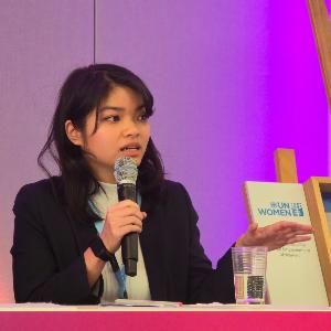 Ban Linh Le speaking with microphone at UN Women panel event with purple backdrop