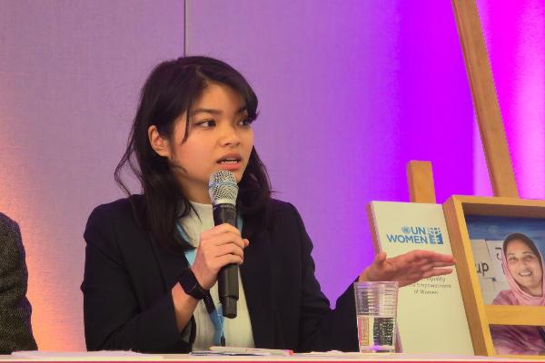 Ban Linh Le speaking with microphone at UN Women panel event with purple backdrop