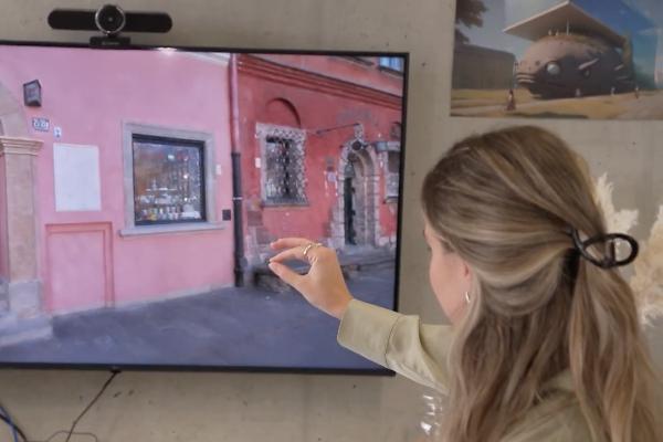 Pauline Leininger interagiert mit großem Bildschirm, zeigt virtuelle Straßenszene in 3D, modernes Smart-Home-Display mit Kamera oben
