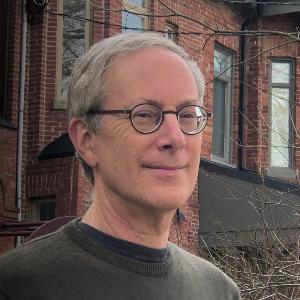 Porträt Professor Penslar im Pullover mit Brille vor einem Backsteinhaus