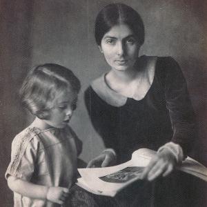 Edith Rosenzweig (sitzend) blickt in die Kamera. Ihr Sohn Rafael steht zu ihrer Rechten und blickt in ein Buch, das seine Mutter auf dem Schoß hält.