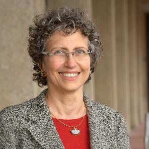 Professor Enrica Piccardo with curly gray hair, glasses, and gray blazer in a professional portrait setting.