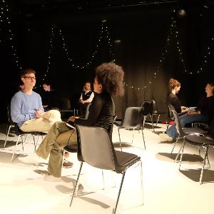 Eine männliche und eine weibliche Person sitzen sich auf einer Theaterbühne gegenüber