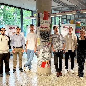 Students and instructors stand side by side in front of panels of the exhibition