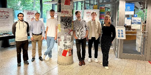 Studierende und Kursleiter stehen nebeneinander vor Tafeln der Ausstellung