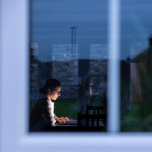 Female entrepreneur using laptop while working during night seen through window model released