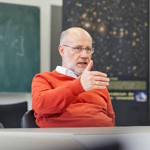 Professor Lesch, Brille, oranger Pullover, gestikulierend im Interview
