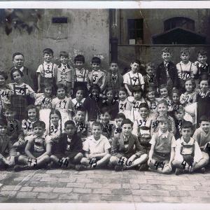 The class photo shows the 48 children and their teacher in front of the Jewish primary school in Herzog-Rudolf-Straße. The children are labelled with numbers to link them to the list of names on the back of the picture.