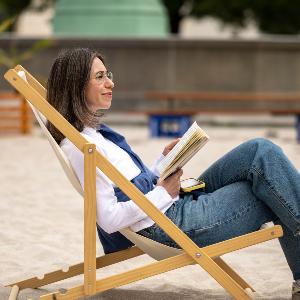 Eine junge Frau sitzt auf einem Liegestuhl und hält ein Buch in der Hand