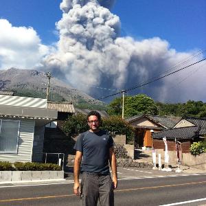 Corrado Cimarelli steht auf einer Straße, im Hintergrung der Vulkan Sakurajima