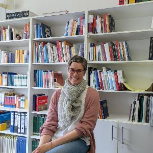 Eine junge Frau sitzt lächelnd vor einer Bücherwand
