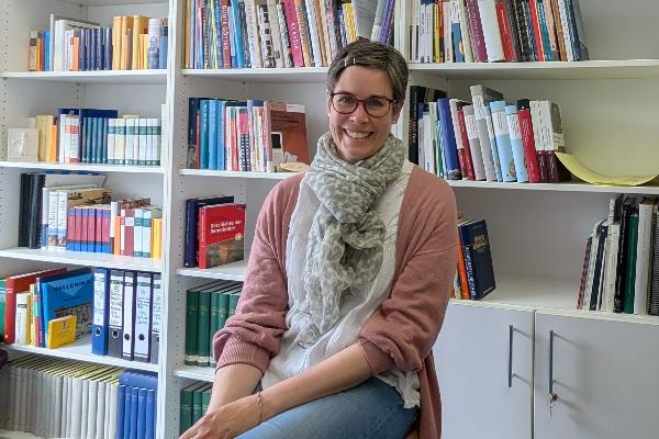 Eine junge Frau sitzt lächelnd vor einer Bücherwand