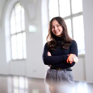 A young woman is standing in front of a window façade in the main building of the LMU.