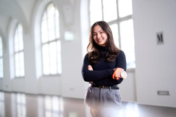 A young woman is standing in front of a window façade in the main building of the LMU.