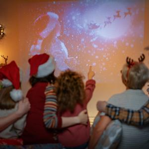 Eine Familie mit Kindern sitzt am Boden und sieht auf einen Bildschirm mit weihnachtlichem Sterne-Motiv.