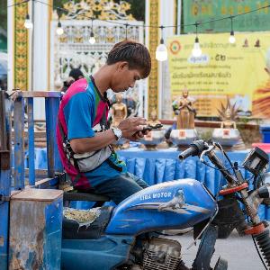 A young man leans against a stationary scooter and looks into a smartphone