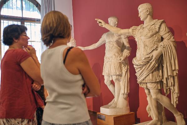 Zwei Frauen stehen vor Abgüssen antiker Statuen im Museum.