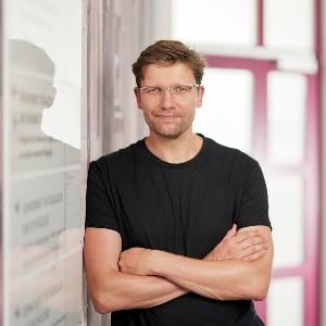 Prof. Markus Gebhardt wears a black T-shirt and glasses and stands next to a magnetic board