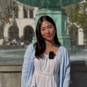 Eine Studentin steht vor dem Brunnen am Geschwister-Scholl-Platz