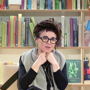 A woman wearing glasses is sitting in front of a bookshelf