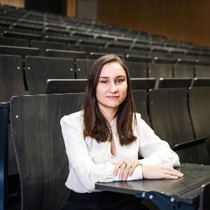 A young woman sits in a lecture hall and looks into the camera.