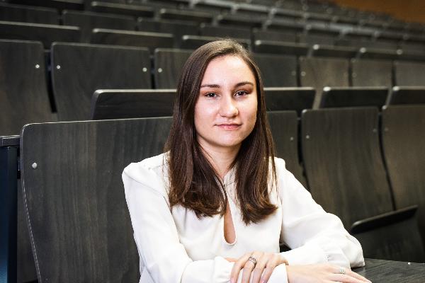 A young woman sits in a lecture hall and looks into the camera.