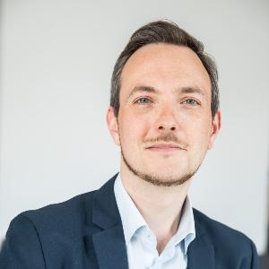 Professor Loy mit blauem Anzug und hellem Hemd vor neutralem Hintergrund