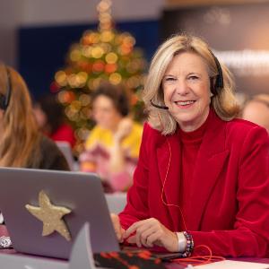 Katja Wildermuth in red blazer with headset working on laptop in a festive call center office.