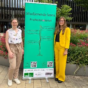 Rebecca Thoss and Anna Axtner-Borsutzky in front of a Freiheit(w)orte roll-up