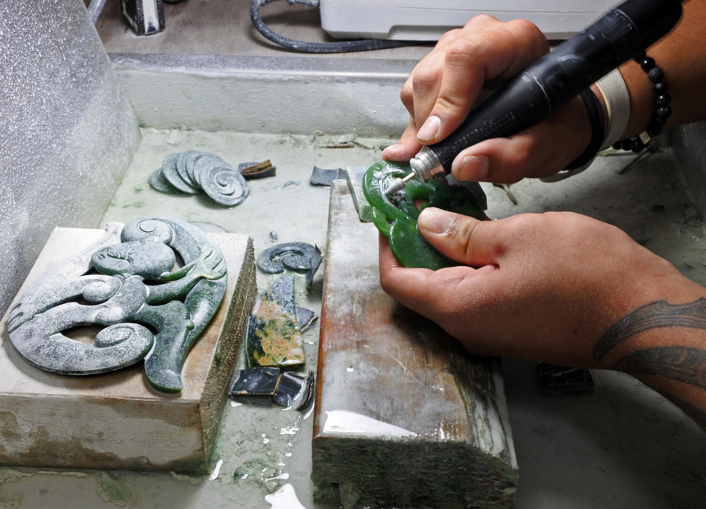 Die Hände eines Bildhauers, der Pounamu bearbeitet. Pounamu steht unter dem Schutz des Vertrags von Waitangi; ihre Gewinnung ist eingeschränkt und wird streng überwacht.