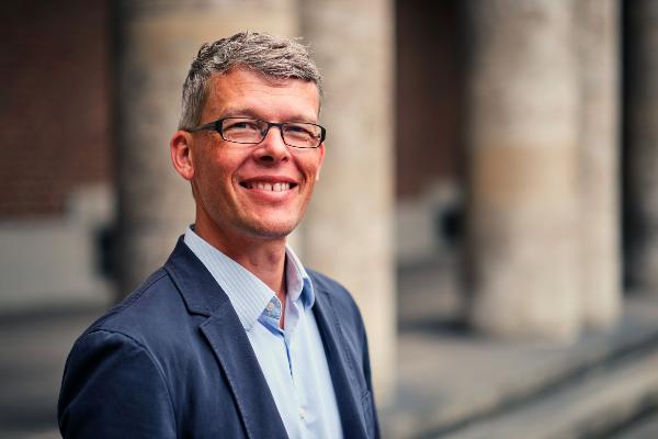 Professor Florian Alt with glasses and gray hair in blue blazer, smiling outdoors in front of columns.