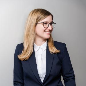 Porträt von Prof. Katja Weidner, Professorin für Lateinische Philologie, im dunkelblauen Anzug und mit Brille.