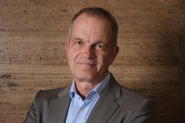 Portrait Professor Christian Walter wearing a grey suit and light blue shirt in front of a natural stone wall.