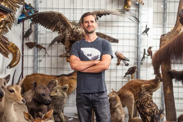Professor Michael Matschiner stands among a collection of preserved animals and birds, surrounded by natural history exhibits.