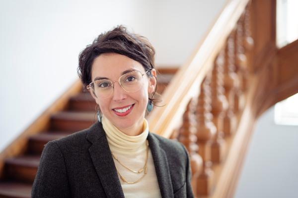 Portrait of Professor Veronika Settele smiling with glasses and blazer standing before a staircase in a bright interior space.