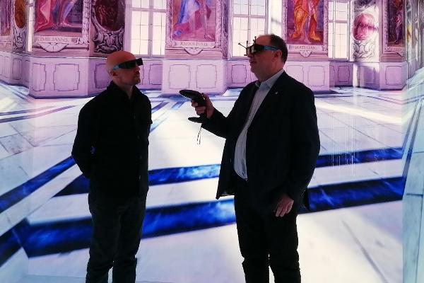 Zwei Männer stehen in einer 3D-Rekonstruktion des Kaisersaals der Residenz Bamberg.