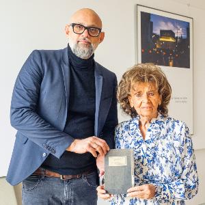 Professor Ronny Vollandt and Charlotte Knobloch are standing next to each other, holding the newly handed-over Hebrew textbook between them.