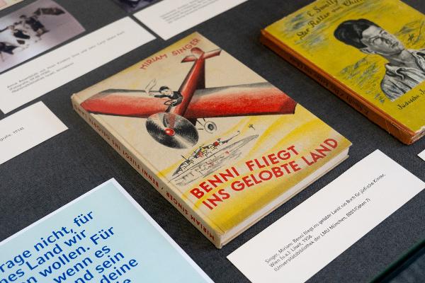 Ausstellungstisch mit dem Kinderbuch „Benni fliegt ins gelobte Land“ von Miriam Singer, illustriert mit rotem Flugzeug und fliegendem Jungen.