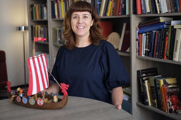 Professorin Verena Höfig vor einem Bücherregal. Vor ihr auf dem Tisch steht ein Winkingerschiff von Playmobil.