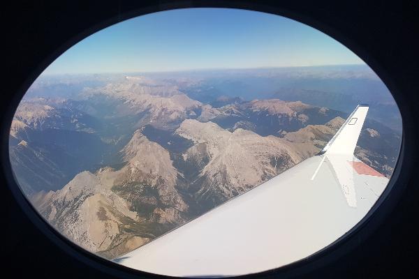 Blick auf die Rocky Mountains aus einem Flugzeugfenster. Die Tragfläche ist zum Teil erkennbar.